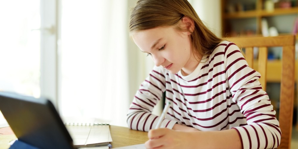 A girl writes her homework at her laptop
